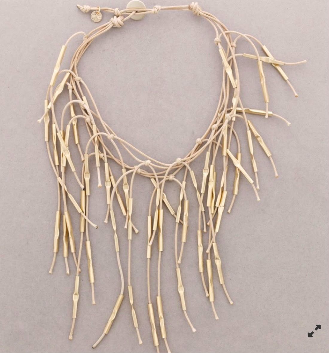 Collar de cuentas color crema con largos hilos colgantes que parecen ramitas sobre un fondo gris claro.