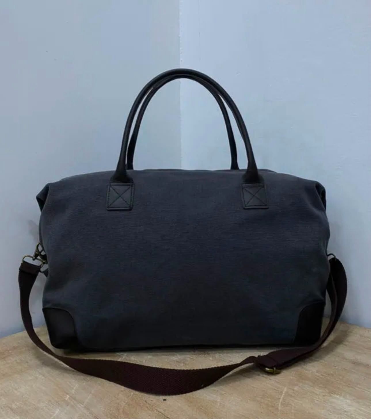 Bolsa de lona azul marino oscuro con correa para el hombro sobre una superficie de madera contra una pared azul claro.