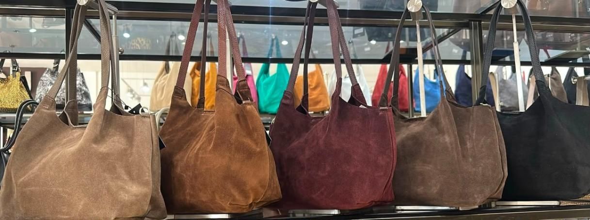 Hilera de bolsos colgados en tonos marrón, tostado, burdeos y azul en un expositor de tienda.