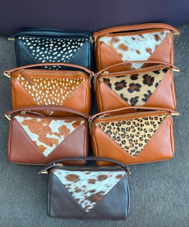 Surtido de pequeñas bolsitas de cuero con solapas de estampado animal, dispuestas sobre una superficie gris.