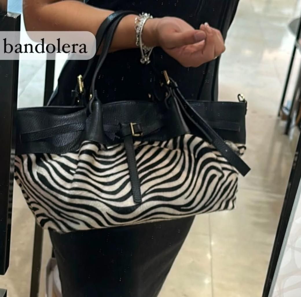Bolso de mano con estampado de cebra en blanco y negro y correas negras, expuesto en una tienda