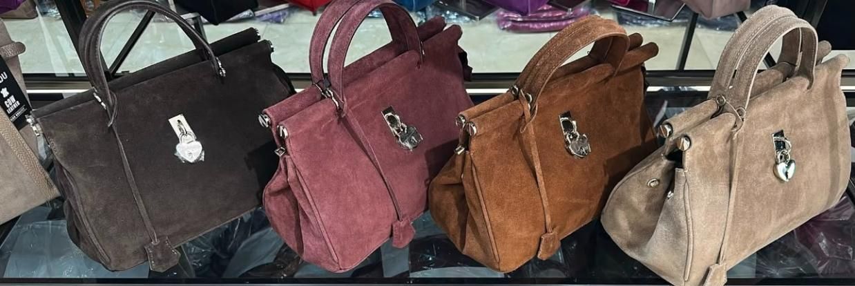 Fila de bolsos en negro, rosa, marrón y beige sobre una mesa de exposición.