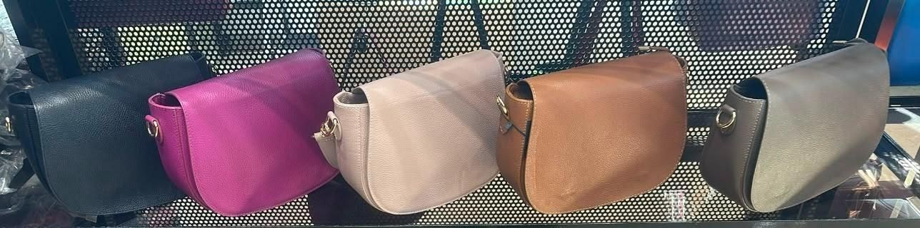 Cuatro bolsos de mano en color magenta, beige, tostado y gris alineados en un estante estampado.