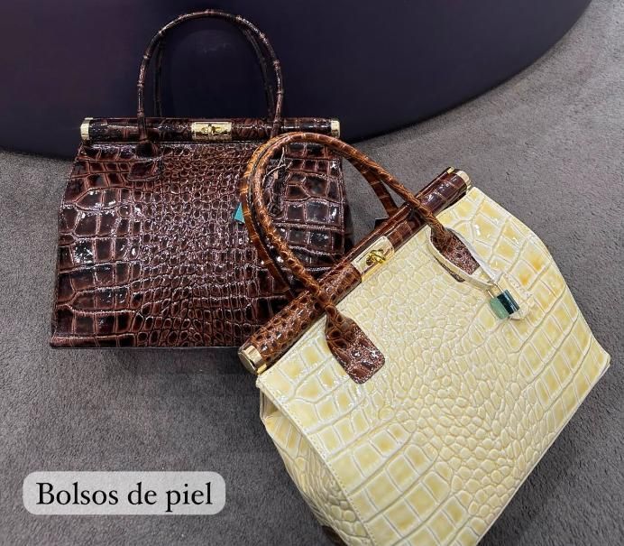 Dos bolsos de piel, uno marrón oscuro y otro beige, con asas sobre fondo oscuro.