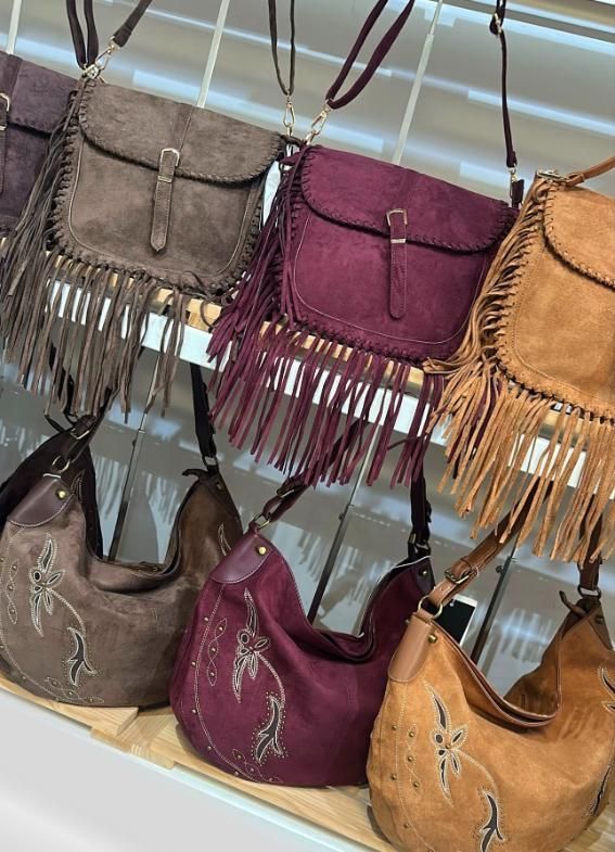 Bolsos de mano coloridos con flecos en tonos tostados, morados, grises y marrones cuelgan de un expositor en una tienda.