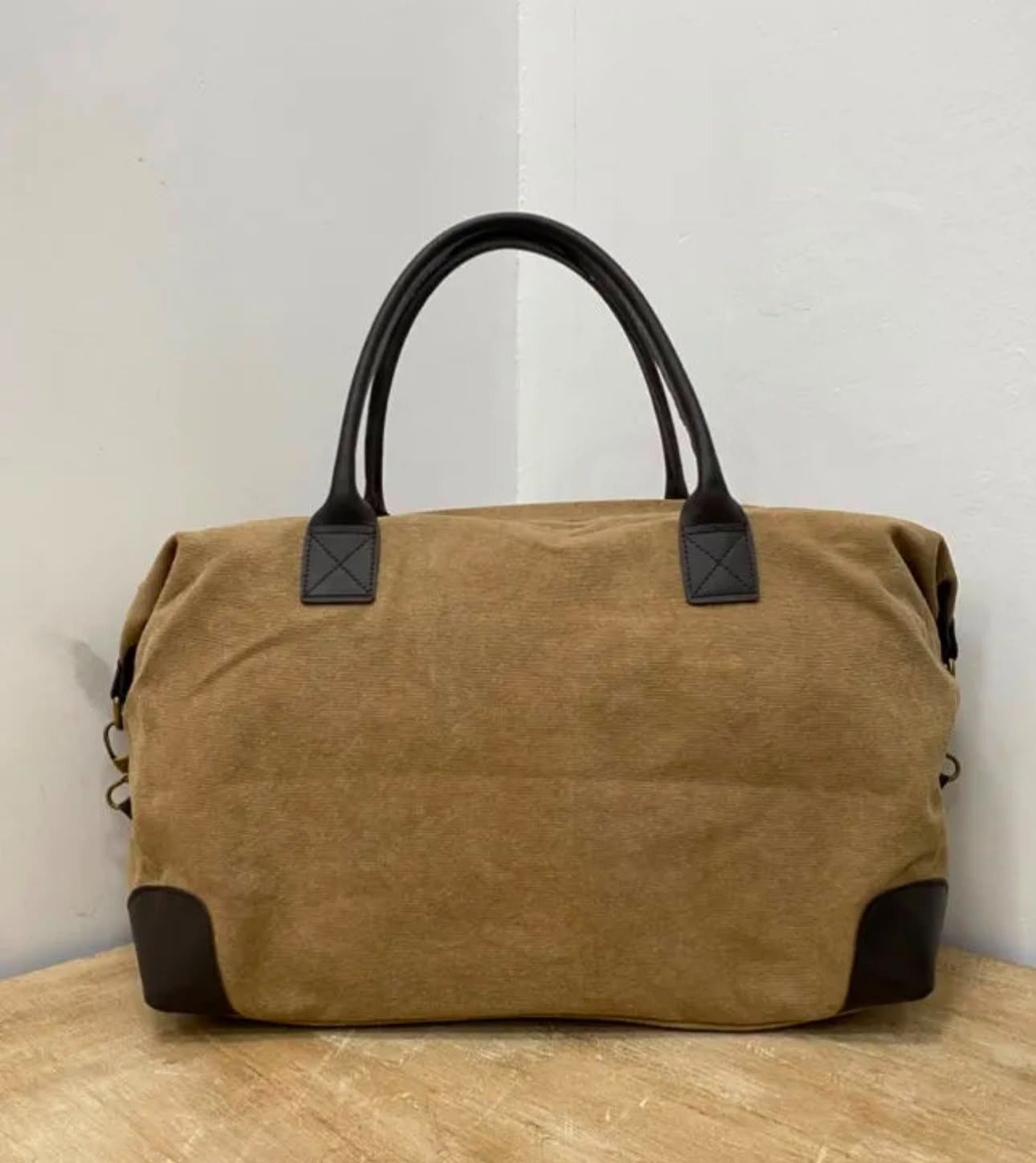 Bolsa de lona marrón con asas negras sobre una mesa de madera contra una pared clara.