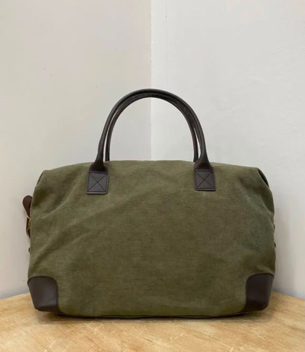 Bolsa de lona verde oliva con asas negras sobre una superficie de madera.
