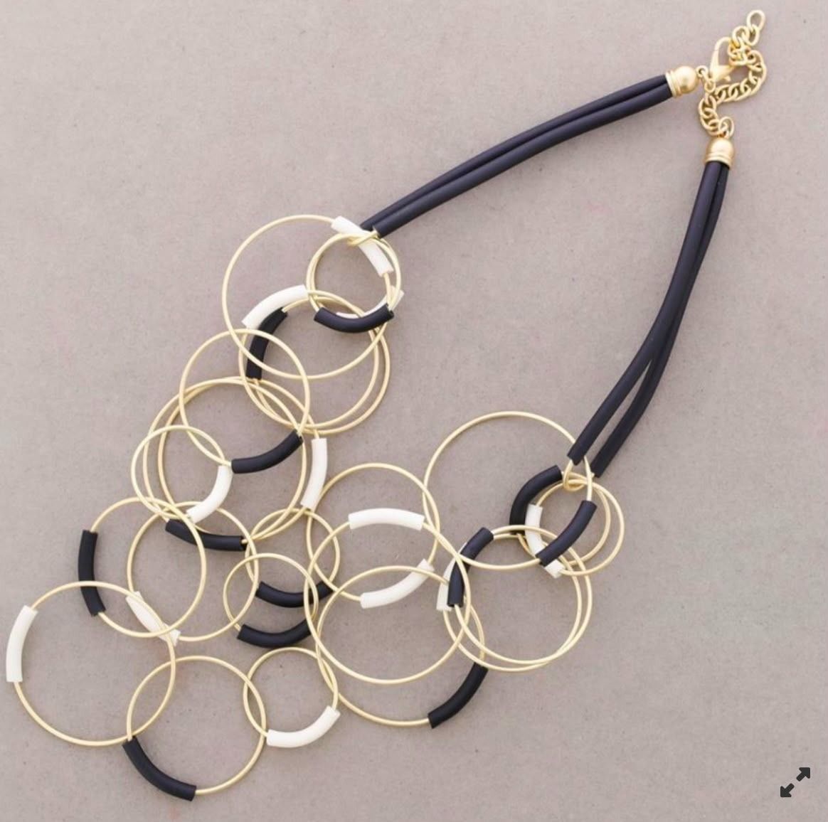 Collar con racimo de anillos dorados y cordones negros sobre fondo gris.