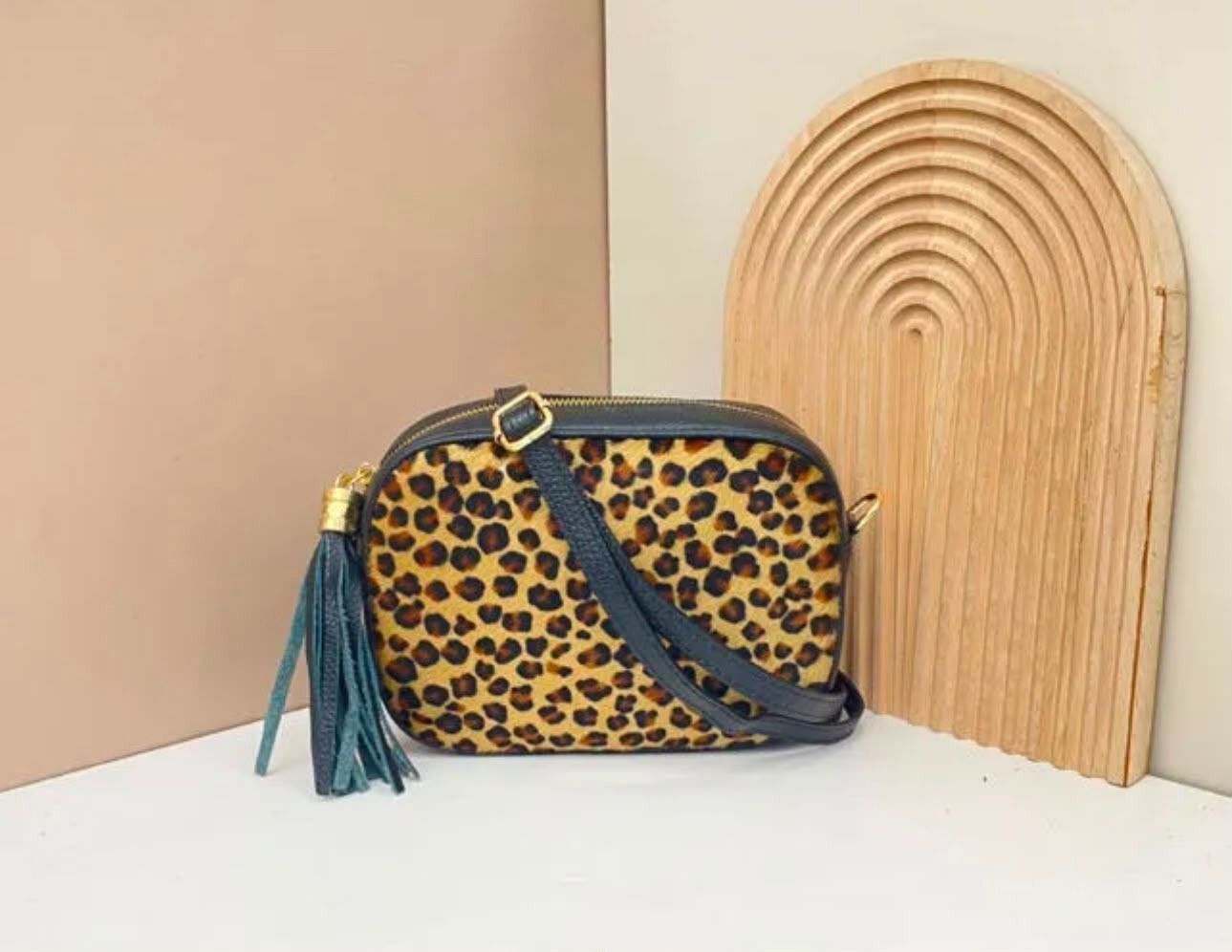 Bolso bandolera con estampado de leopardo, correa color turquesa y borla sobre una mesa blanca