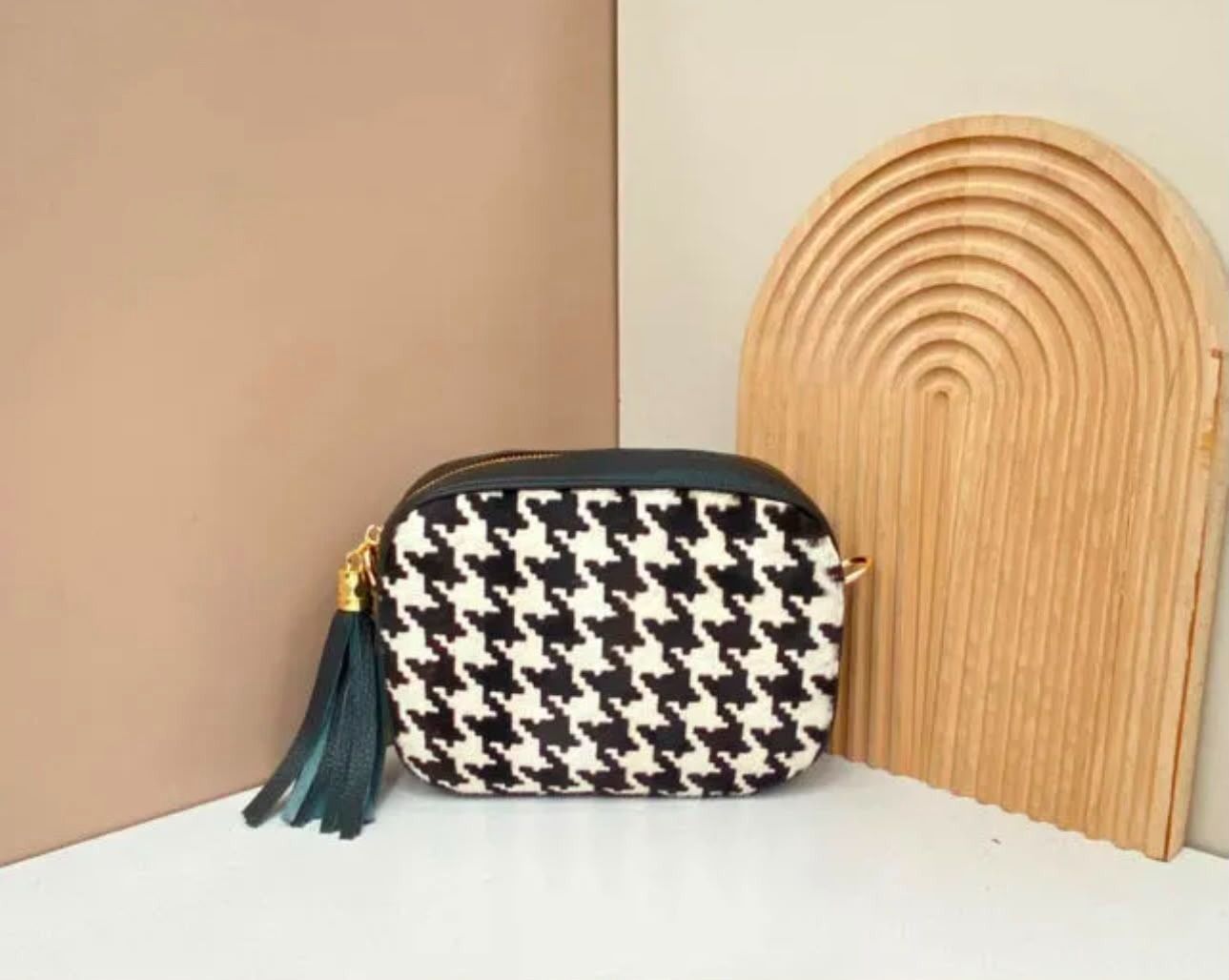 Bolso de mano blanco y negro con estampado de pata de gallo y borla turquesa junto a un arco decorativo de madera.