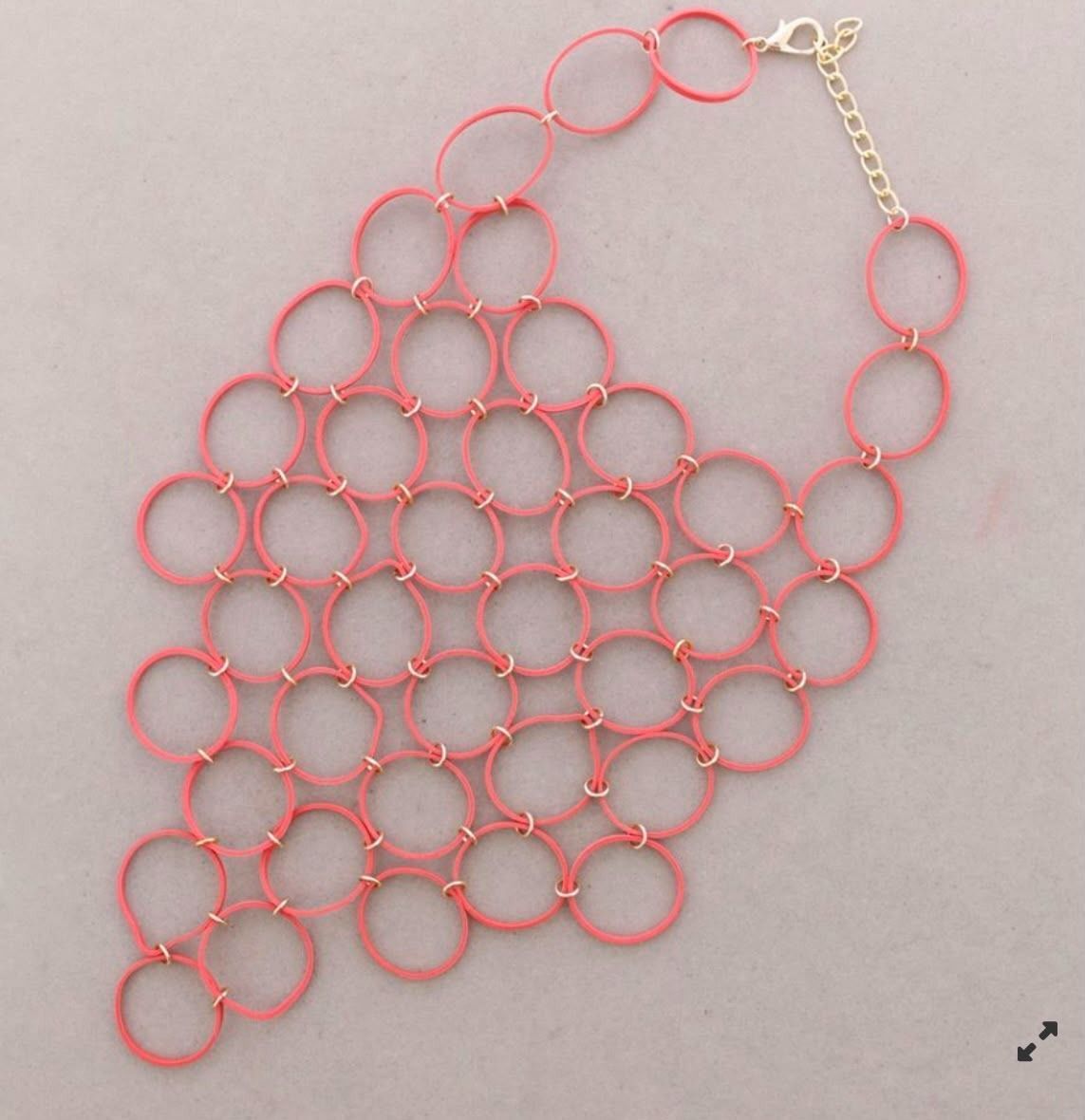 Collar de cuentas rosas con anillos circulares entrelazados sobre un fondo gris claro.