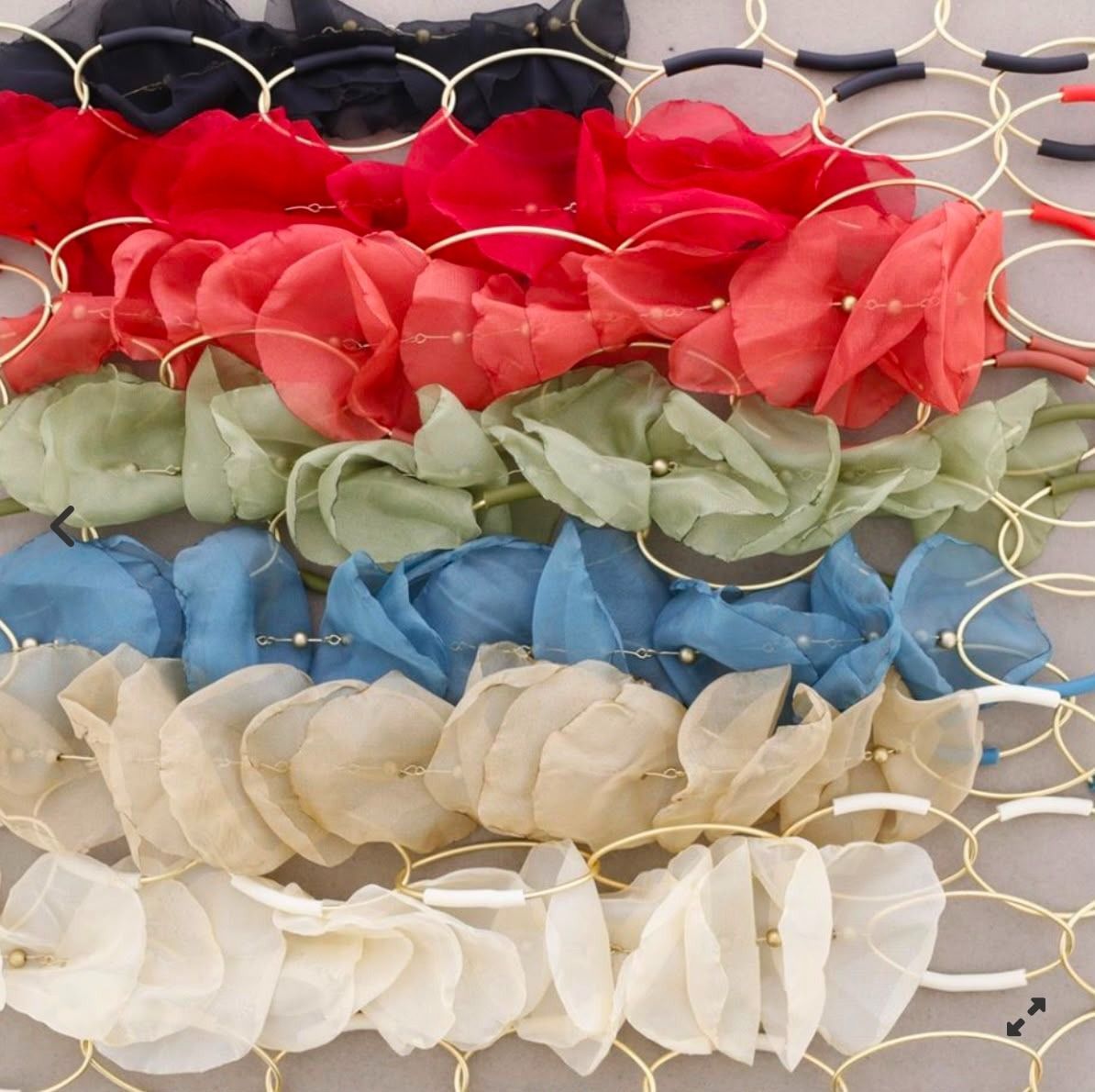 Hileras de pétalos de flores de colores extendidas sobre una cerca de alambre: rojo, verde, azul y blanco.