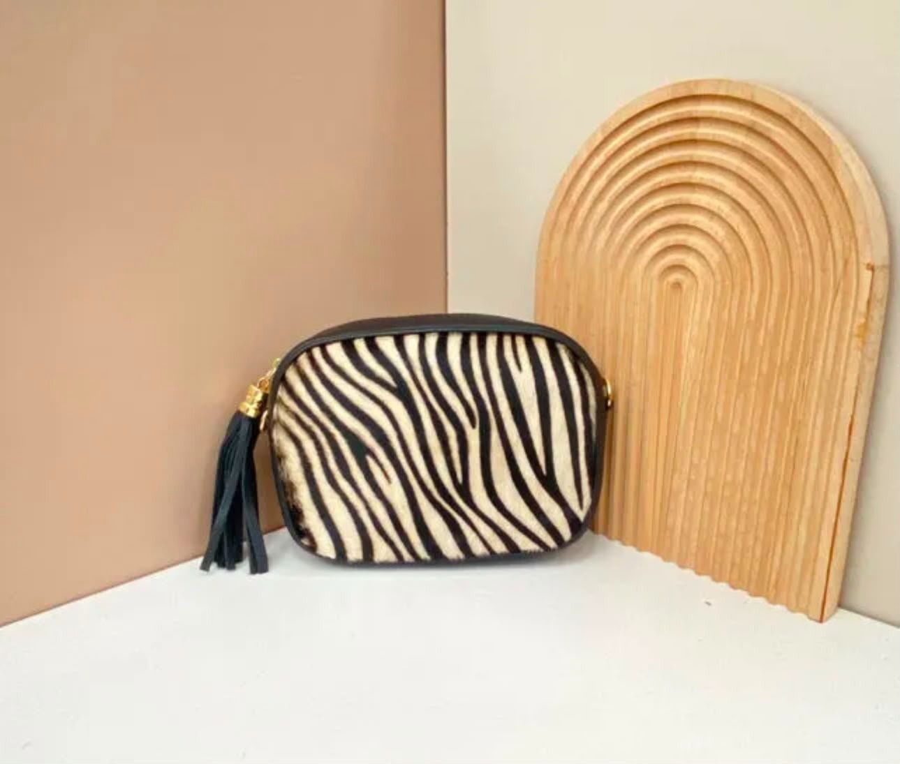 Bolso con estampado de cebra junto a un bolso de mano tejido color canela sobre una superficie blanca contra paredes beige.