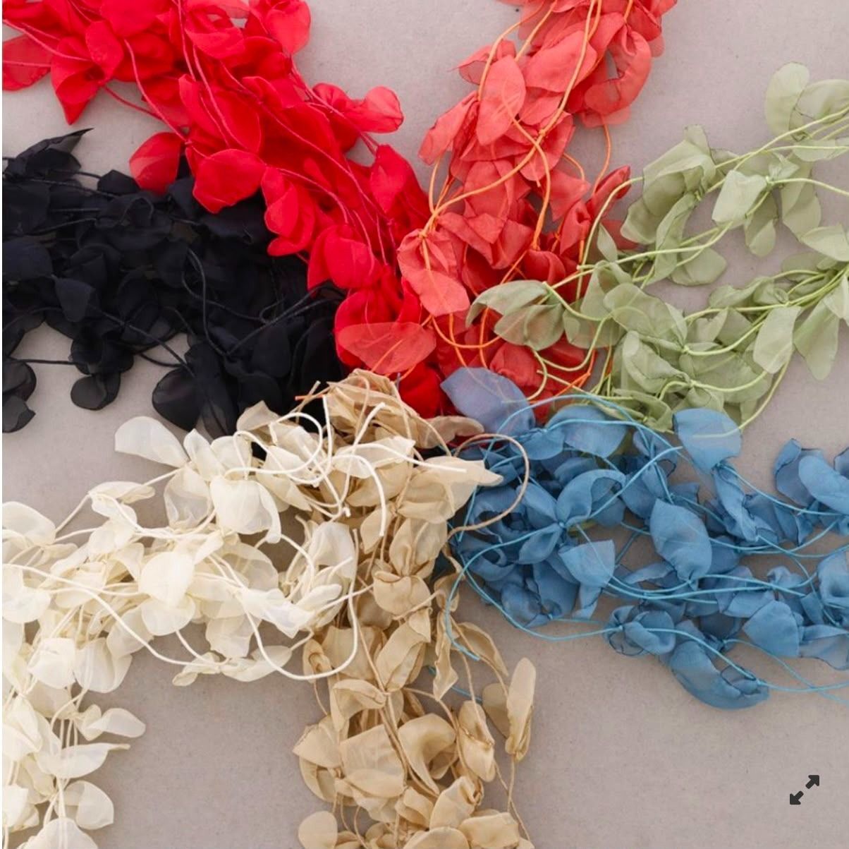 Flores de cinta de colores variados en rojo, rosa, verde, negro, blanco, beige y azul sobre una superficie clara.