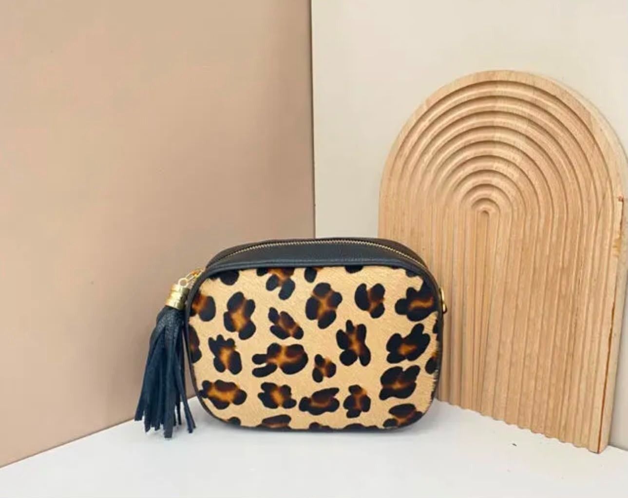Bolsita con cremallera y estampado de leopardo con borla azul marino junto a una pieza decorativa de madera