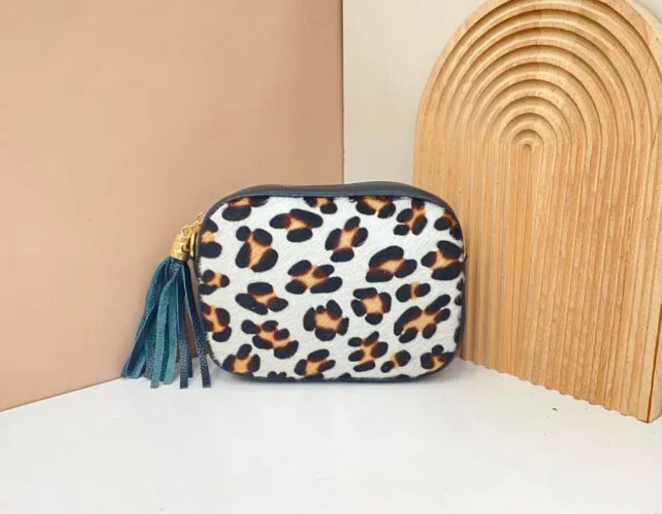 Bolsita con estampado de leopardo y borla color turquesa junto a un arco de mimbre sobre una superficie blanca.