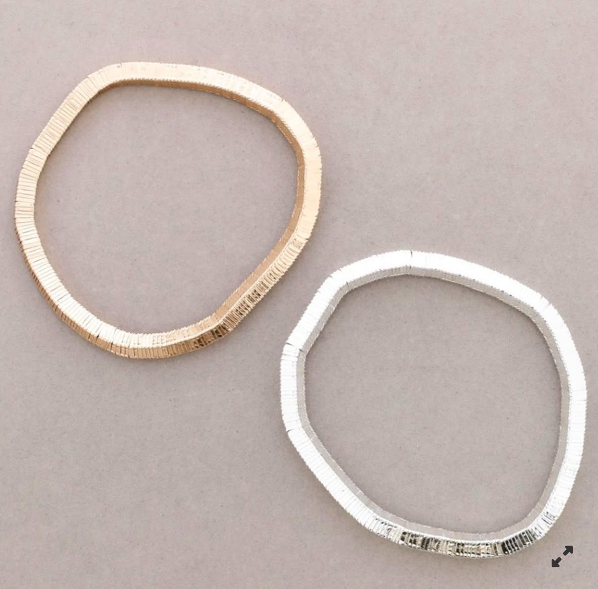 Dos sencillas gomas elásticas para el pelo, una beige y otra blanca, sobre un fondo gris liso.
