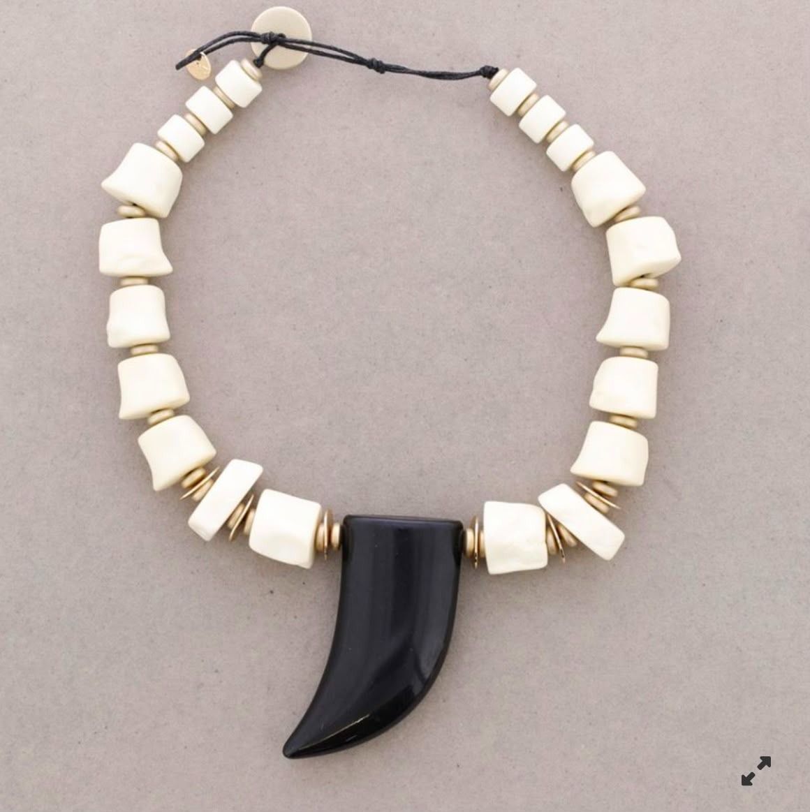 Collar de cuentas blancas con un colgante negro en forma de garra sobre un fondo gris.