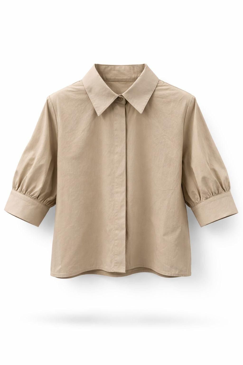 Camisa beige de manga corta con botones, cuello de pico y puños, mostrada sobre fondo blanco.