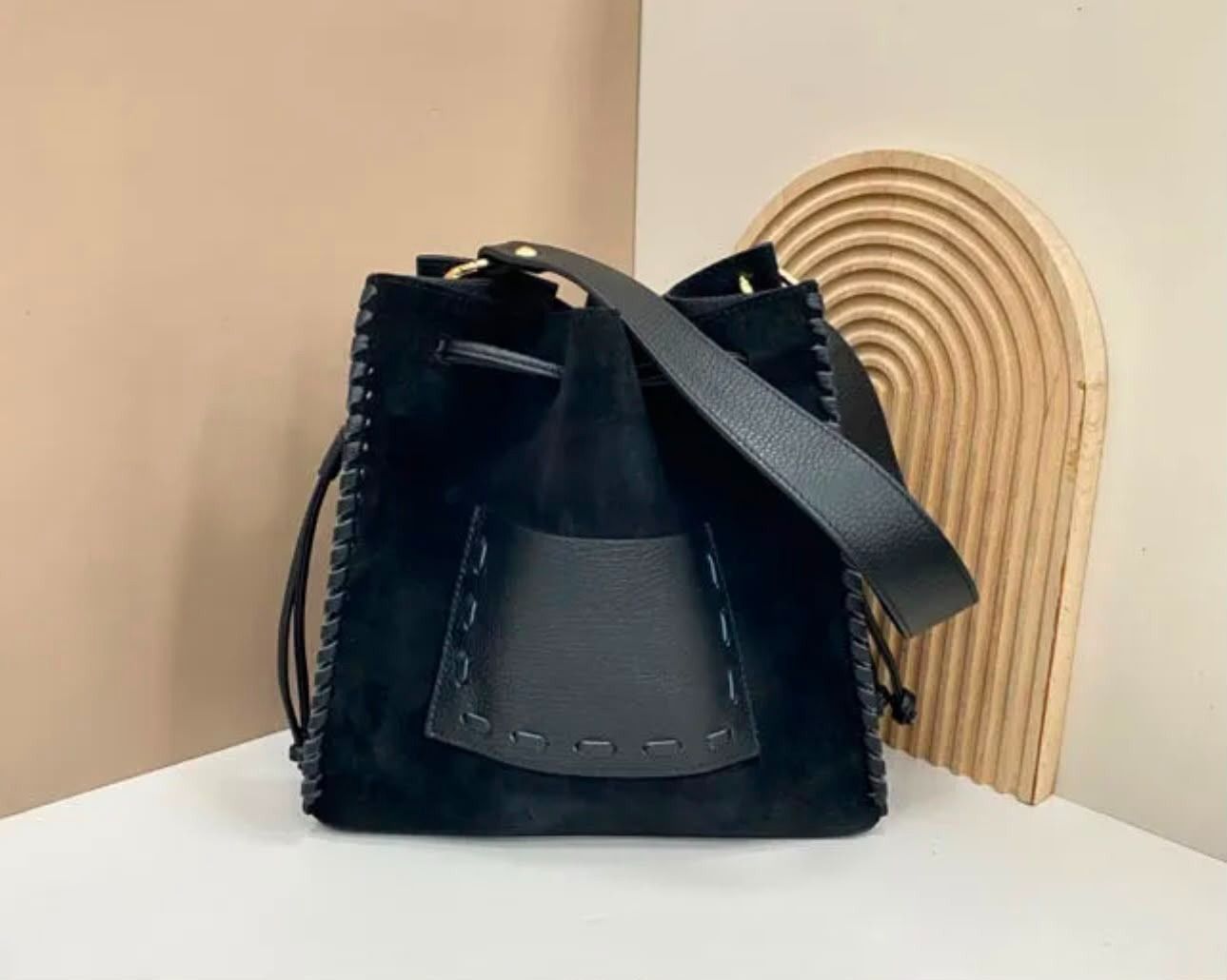 Bolso tipo cubo de piel negra con correa para el hombro y panel decorativo tejido de color beige.