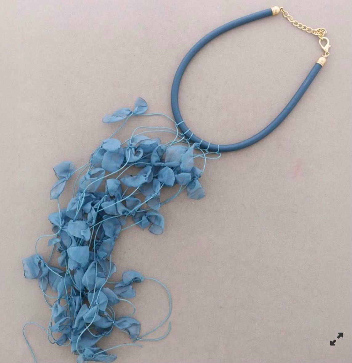 Collar azul con un grupo de piezas florales translúcidas en cascada sobre un fondo gris.