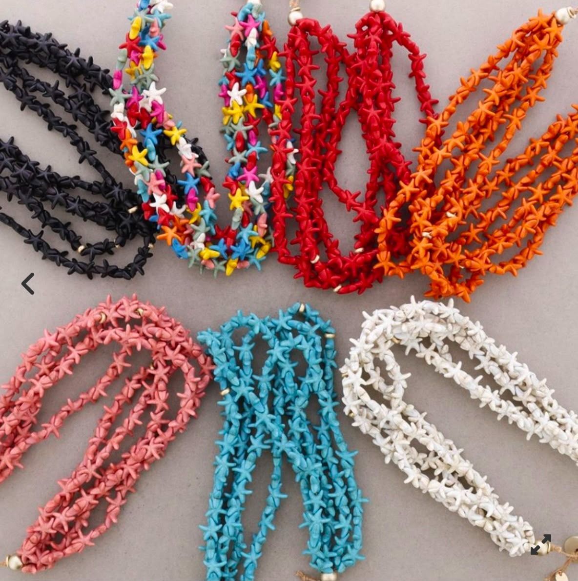 Pulseras coloridas en forma de estrella en negro, multicolor, rojo, naranja, rosa, azul y blanco sobre una superficie gris.