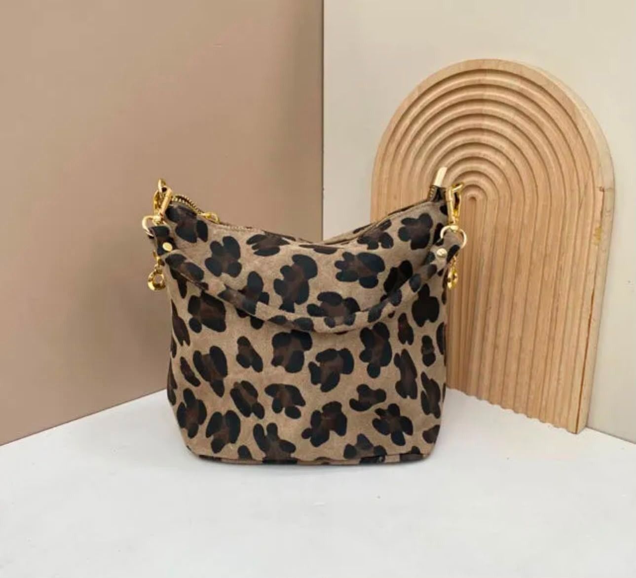 Bolso con estampado de leopardo sobre una mesa blanca junto a un arco de madera curvado.