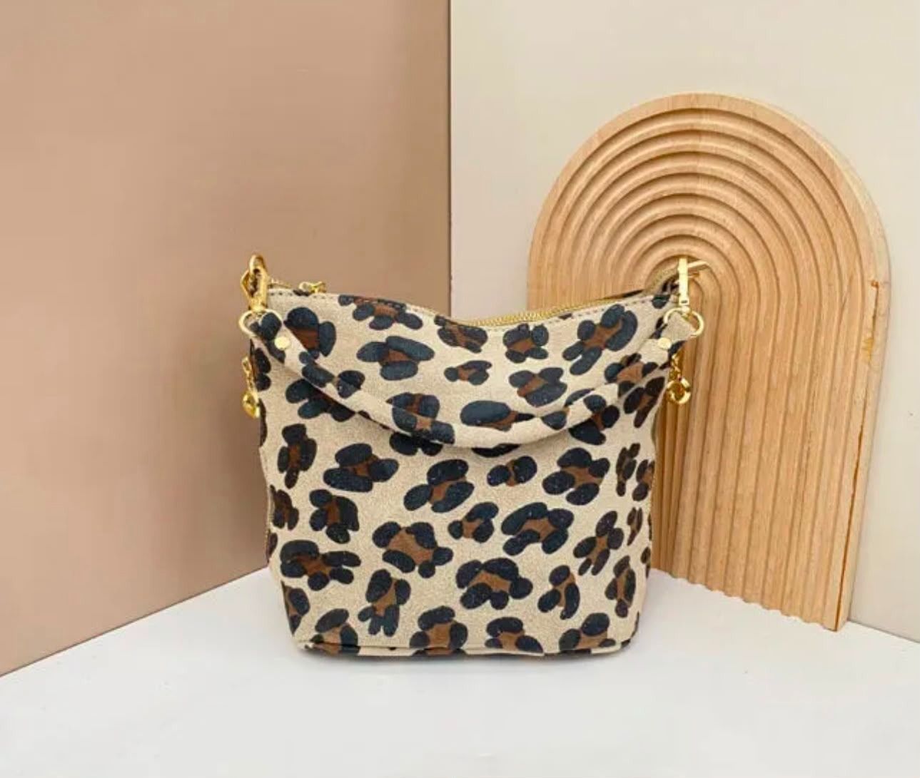 Bolso con estampado de leopardo y cadena dorada sobre una superficie blanca junto a un arco decorativo tejido.