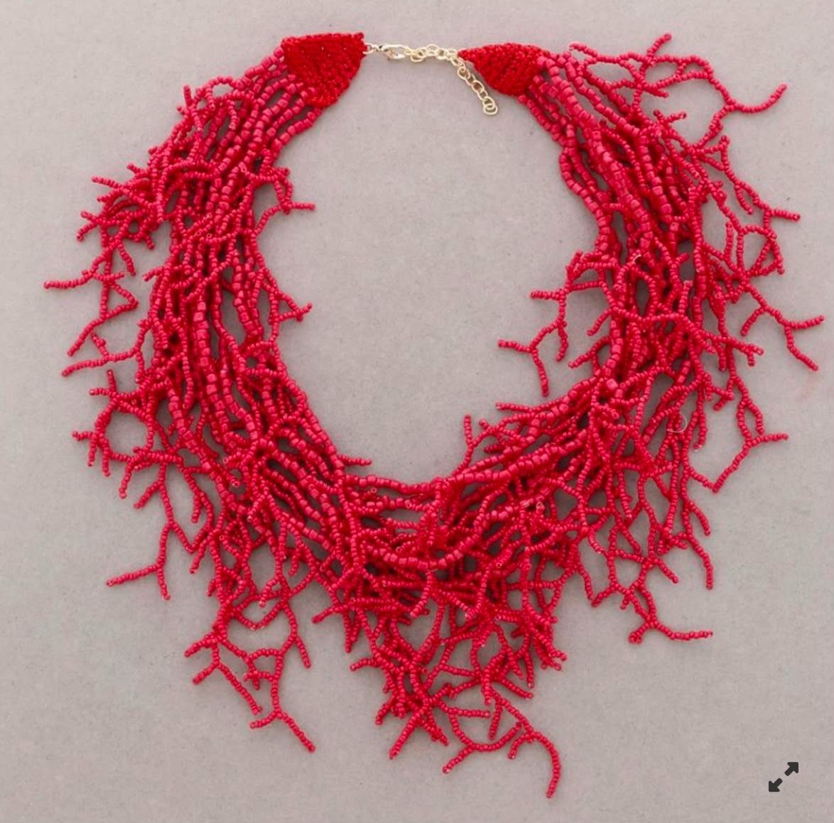 Collar de cuentas rojas con hilos colgantes que imitan el coral sobre un fondo claro.