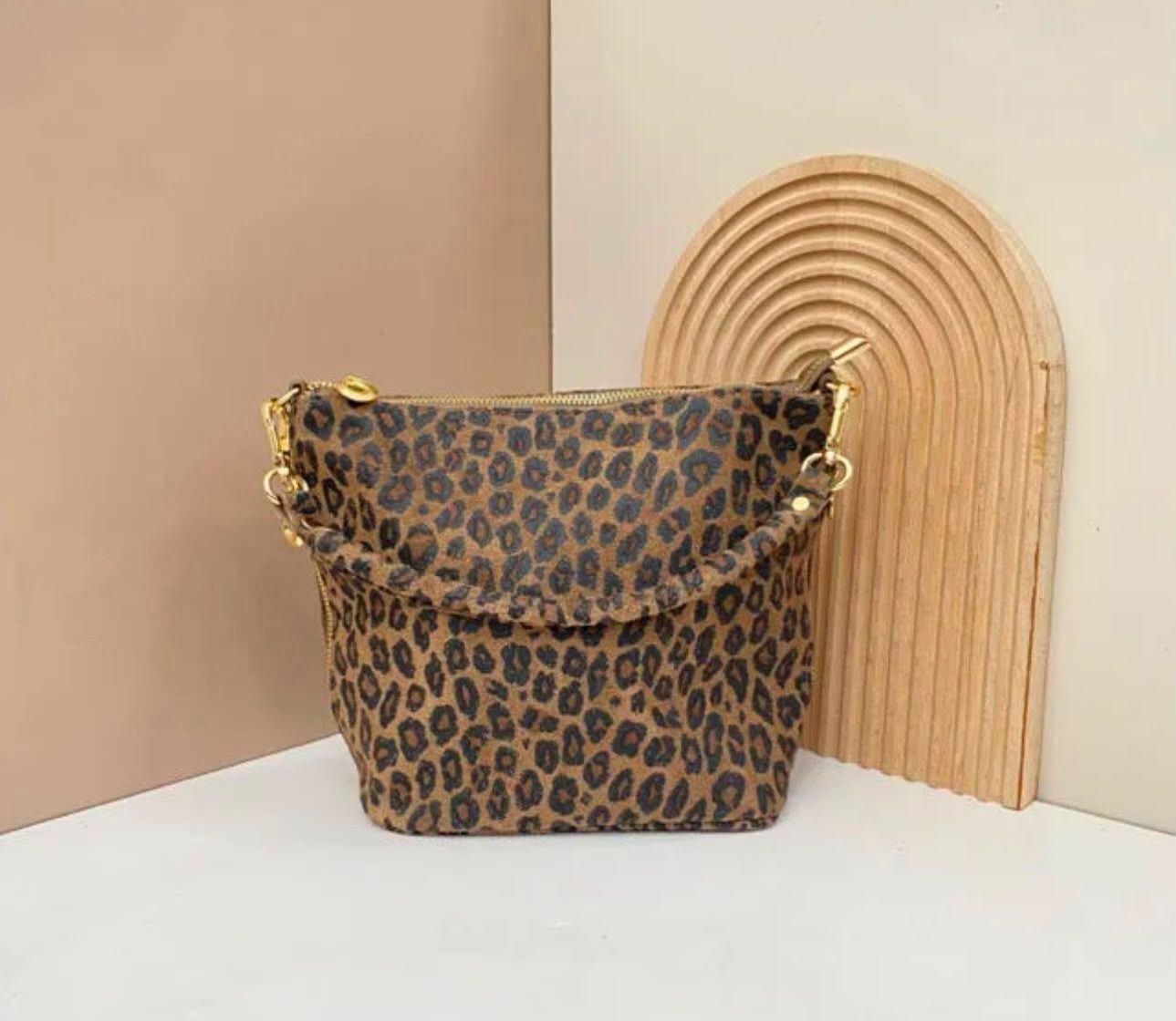 Bolso con estampado de leopardo sobre una superficie blanca junto a una pieza decorativa arqueada de color tostado.