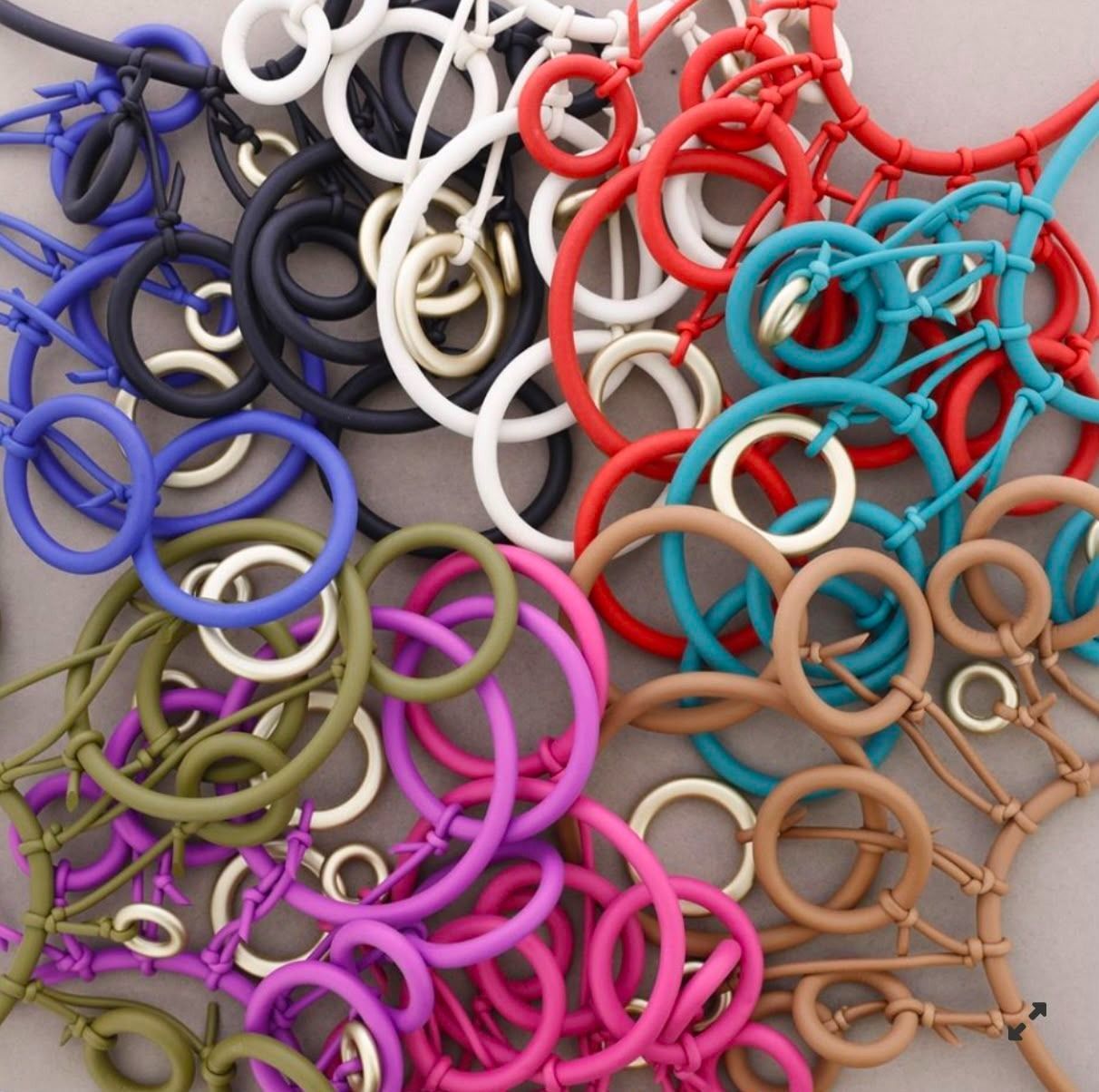 Varios anillos de colores y llaveros circulares esparcidos en un montón sobre una superficie neutra.