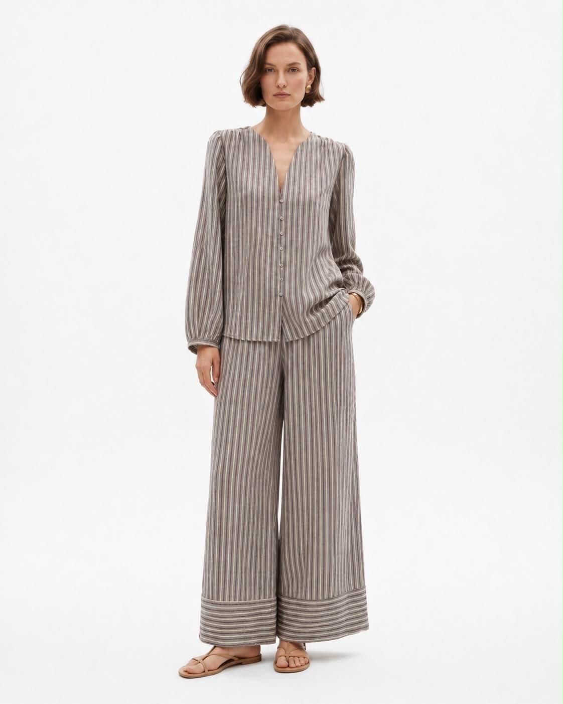Modelo con blusa de rayas grises y pantalones de pierna ancha sobre fondo blanco.