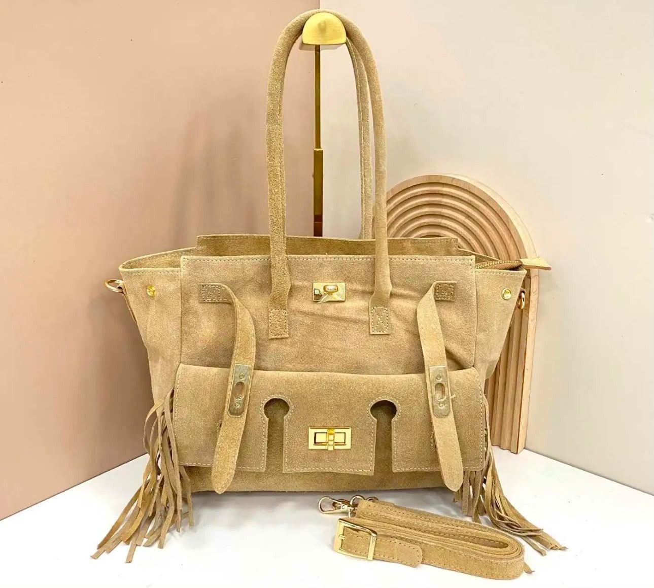 Bolso tote tejido color beige con asas largas, detalles de flecos y correa a juego sobre un fondo claro.