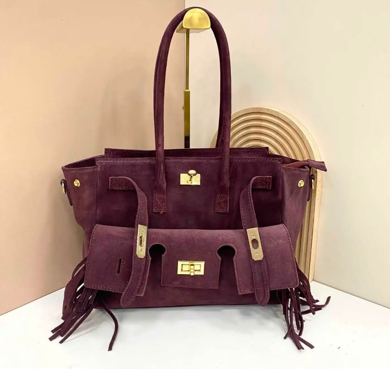 Bolso de mano de ante morado con detalles de flecos, mostrado sobre una superficie blanca con fondo claro.
