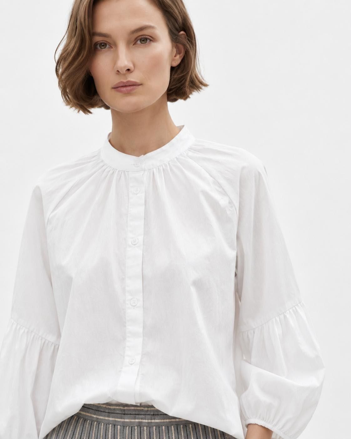 Mujer con blusa blanca de mangas abullonadas sobre un fondo liso.