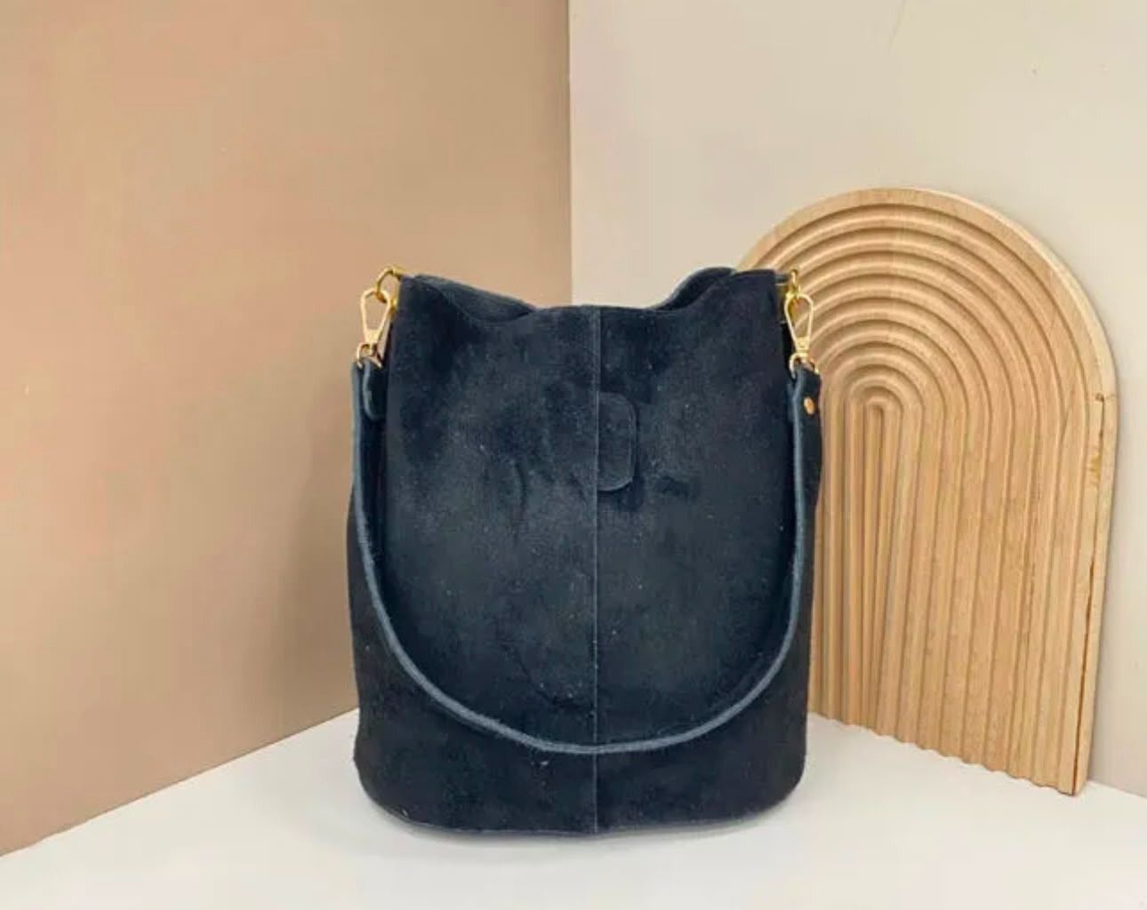 Bolso cubo de gamuza azul marino sobre una superficie blanca junto a un arco de madera decorativo