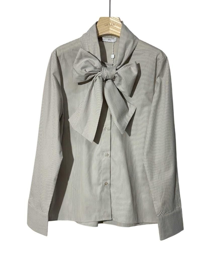 Blusa gris claro a rayas con cuello de pajarita, colgada en una percha.