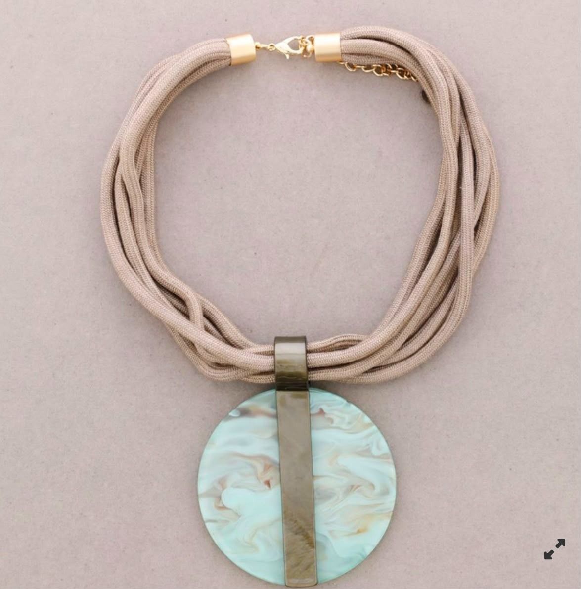 Collar beige de varias hebras con colgante circular jaspeado turquesa y barra decorativa dorada.