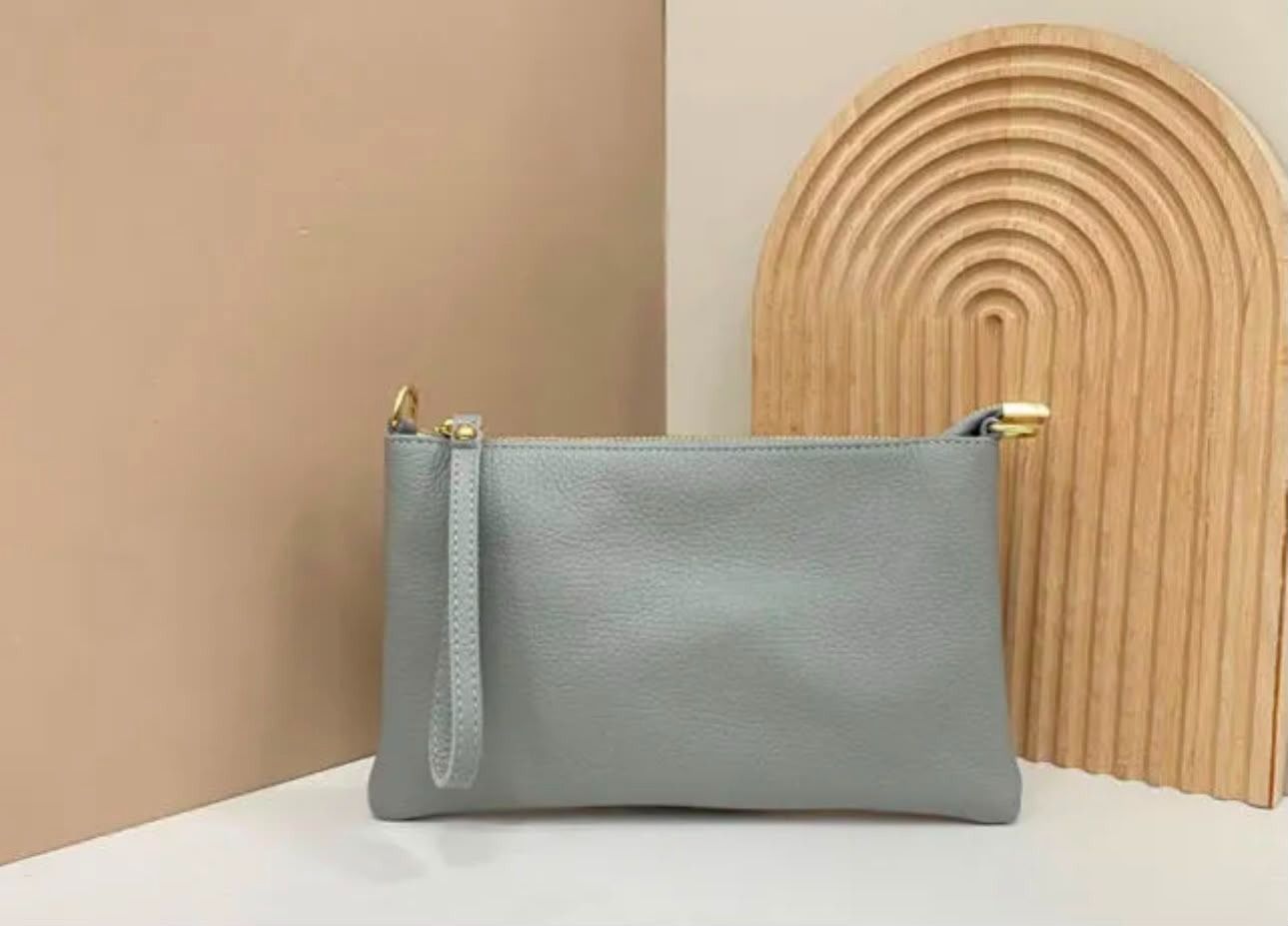 Un estuche gris claro con cremallera sobre una superficie blanca junto a un arco decorativo de madera.