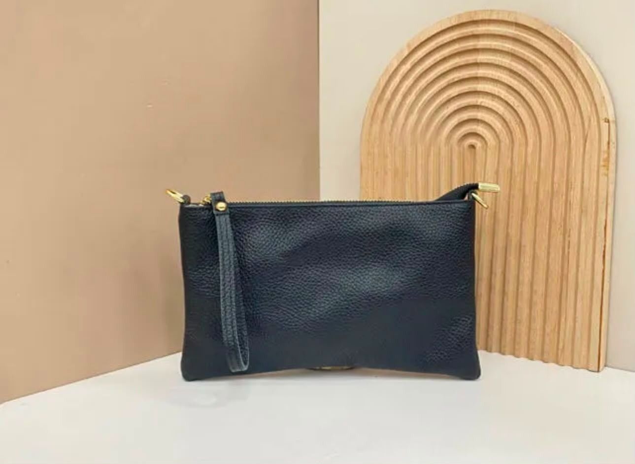 Bolsita negra texturizada con cremallera dorada junto a una pieza decorativa de madera arqueada sobre una superficie blanca.