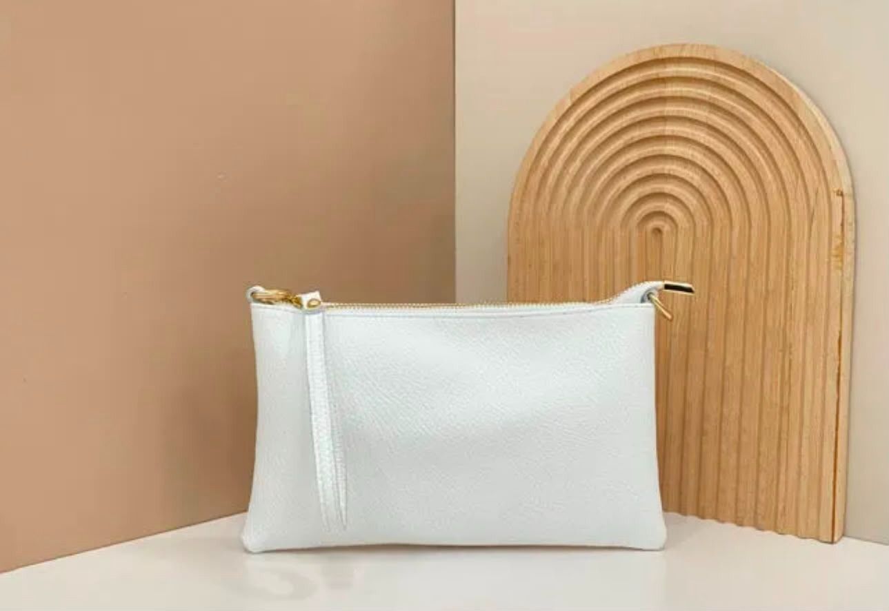 Bolsita blanca con cremallera sobre una superficie beige junto a una pieza decorativa de madera redondeada.