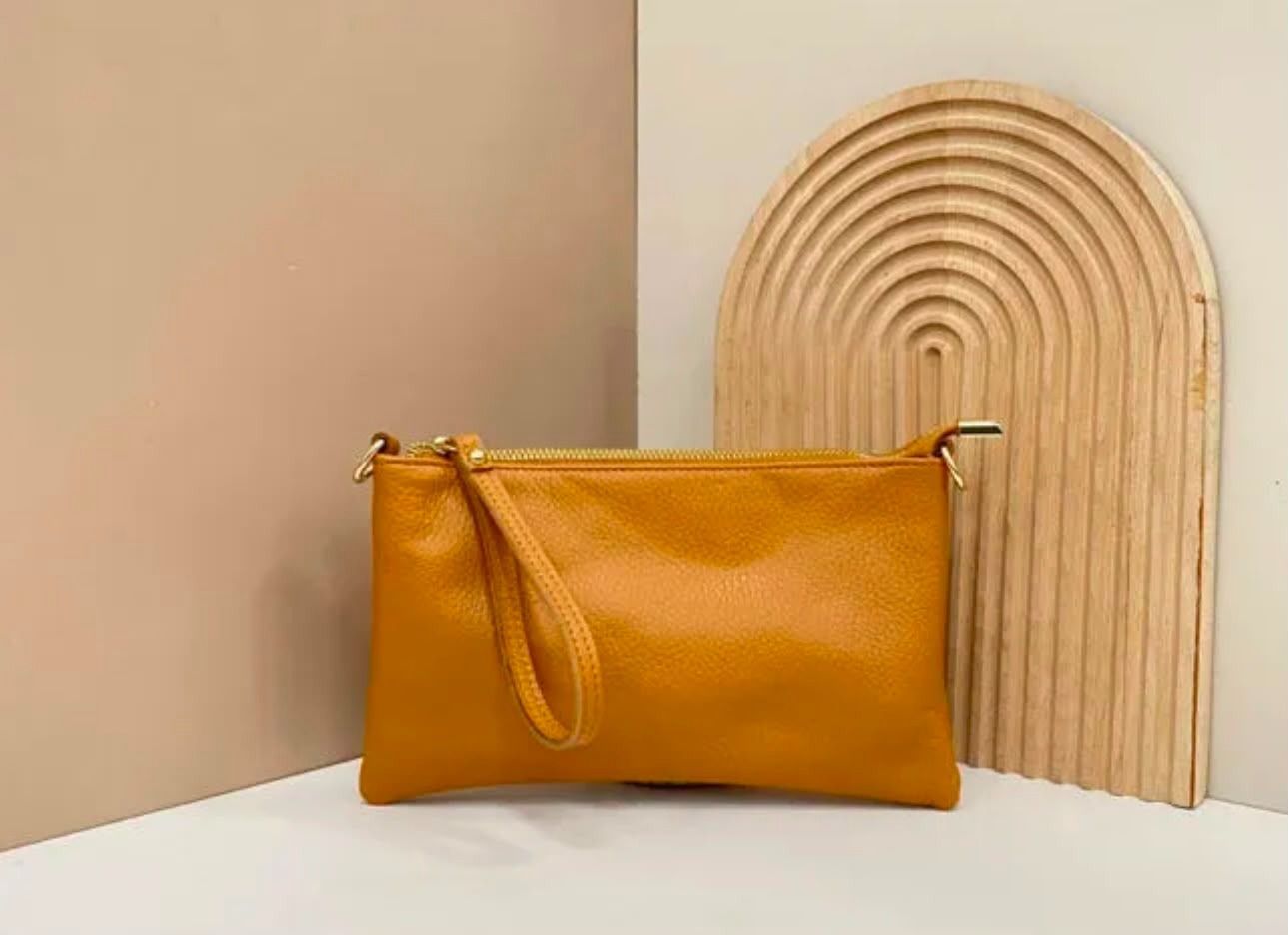 Una bolsita de color amarillo mostaza sobre una superficie blanca, junto a un panel decorativo arqueado de madera clara.