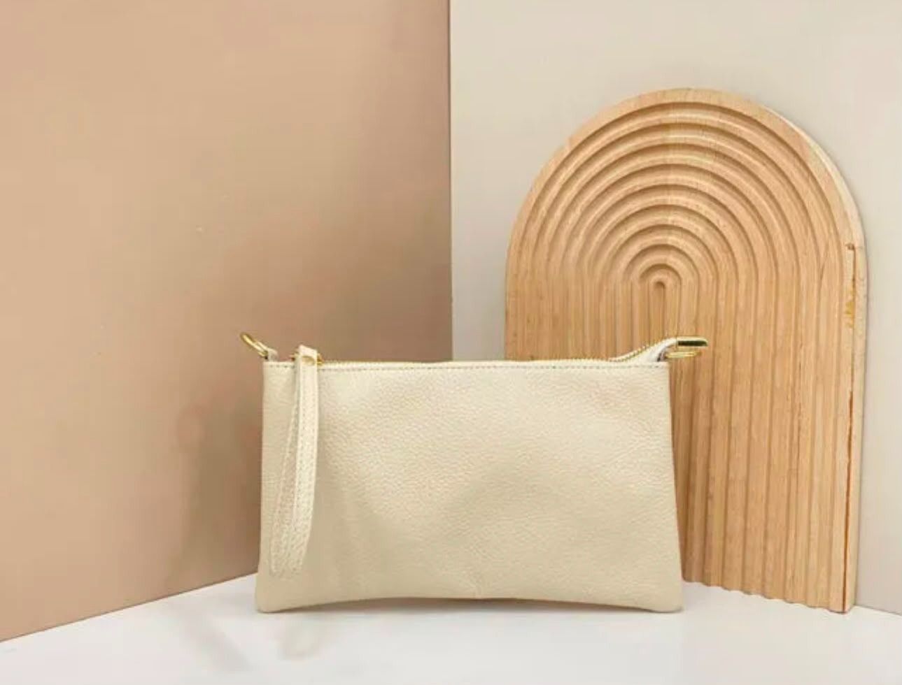 Un neceser color crema con cremallera sobre una superficie blanca, junto a una pieza decorativa de ratán arqueada
