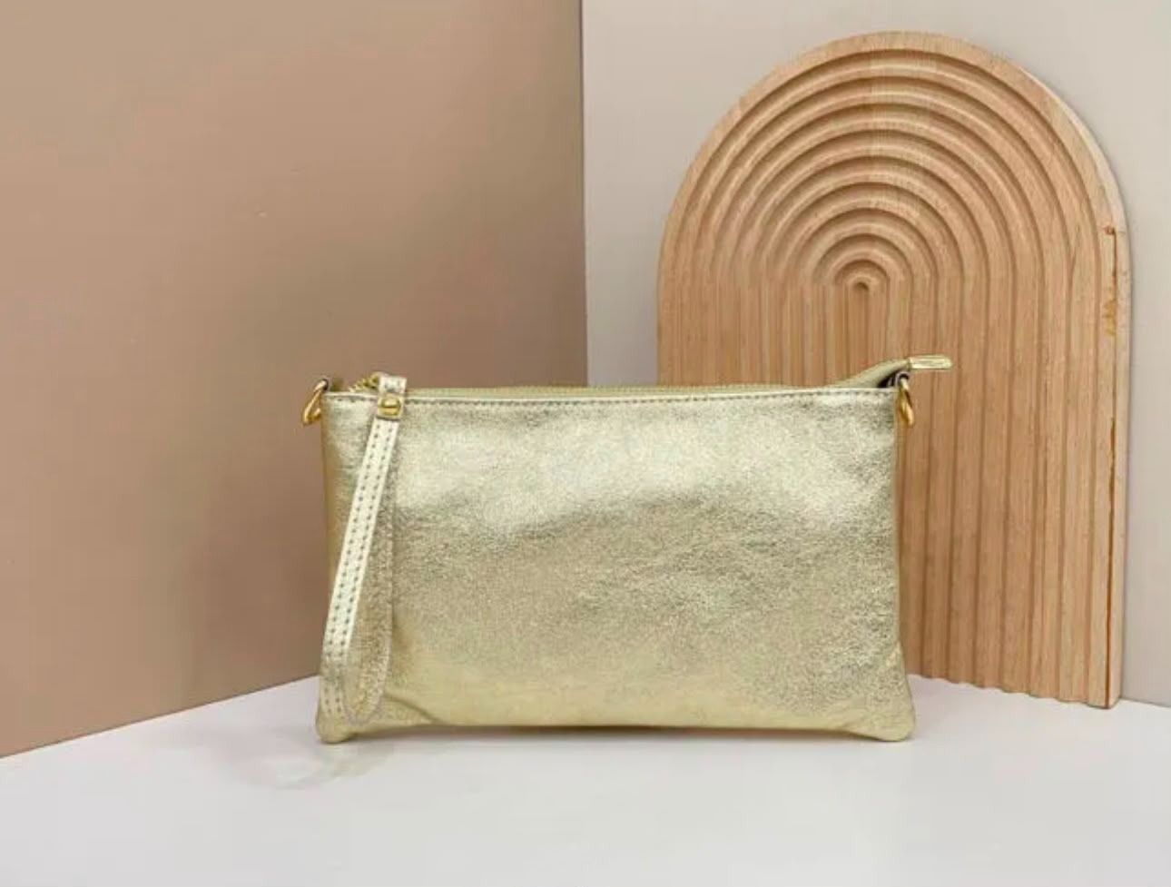 Un bolso de mano dorado sobre una superficie blanca junto a un panel decorativo de madera curvado.