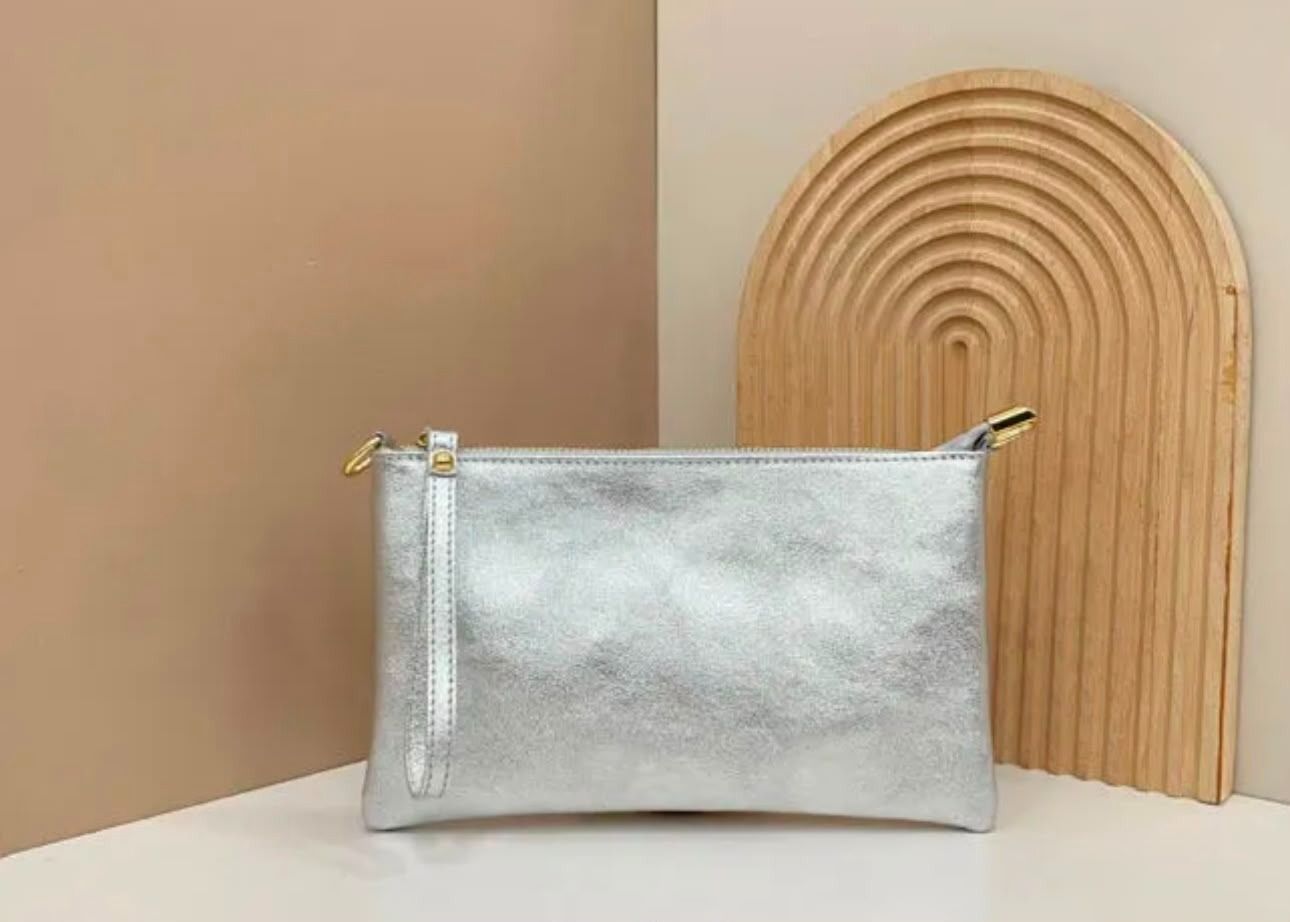Un bolso de mano plateado sobre una mesa blanca contra una pared beige, con un arco de madera tejido como telón de fondo.