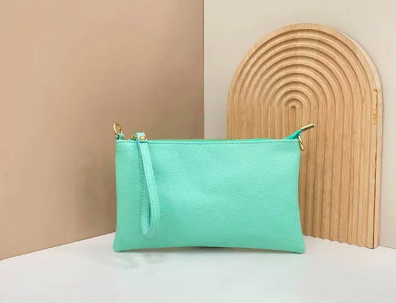 Bolsita verde menta sobre una superficie blanca junto a un panel decorativo de arco de ratán tejido.