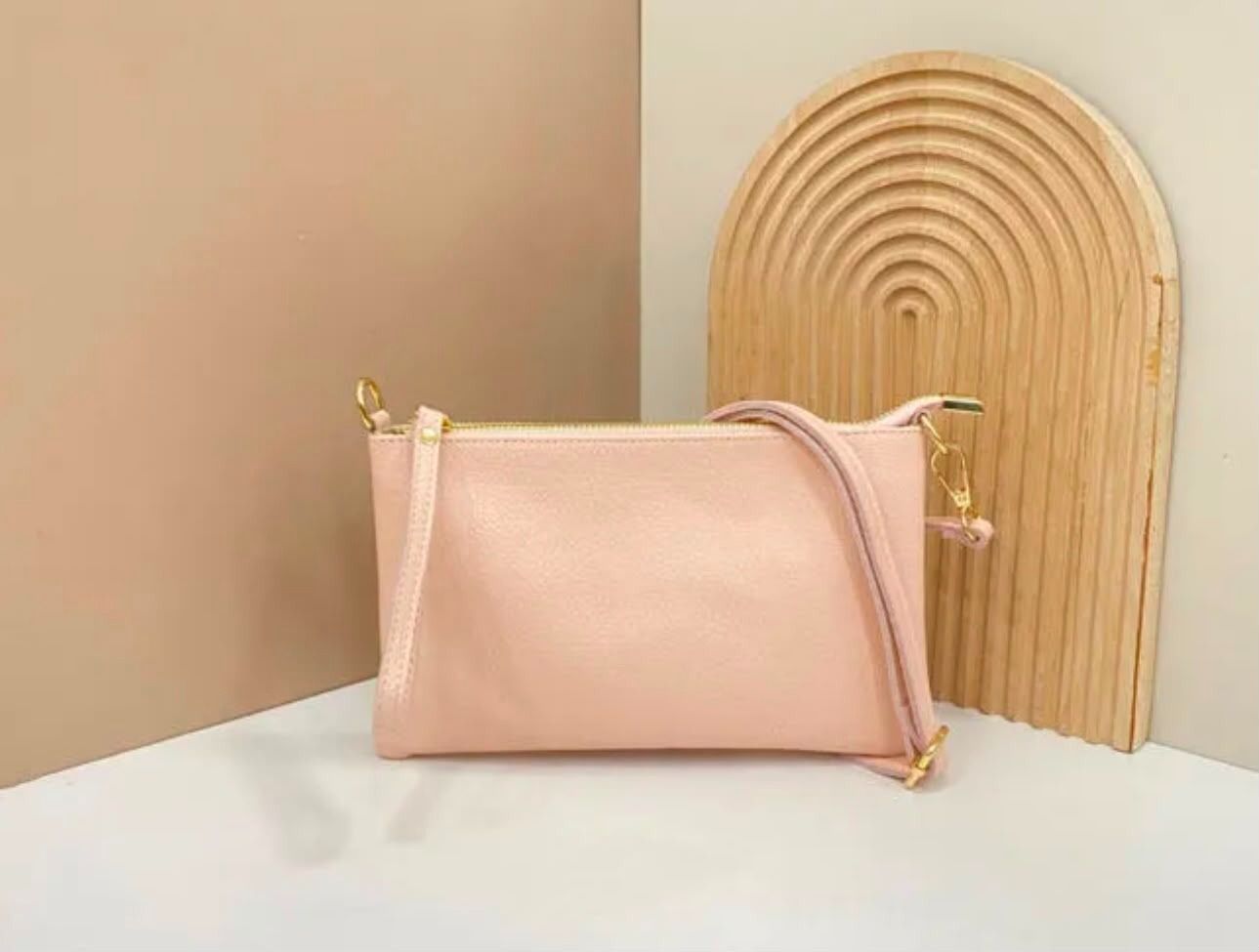 Un bolso rosa sobre una superficie blanca junto a una pieza decorativa de madera arqueada contra una pared beige.