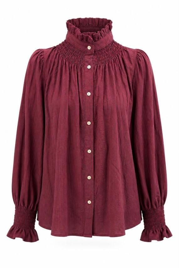 Blusa burdeos de manga larga con volantes, cuello alto fruncido y puños abotonados.