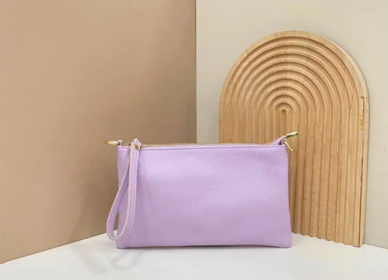 Bolso de mano color lavanda sobre una superficie blanca junto a un panel decorativo de arco tejido.