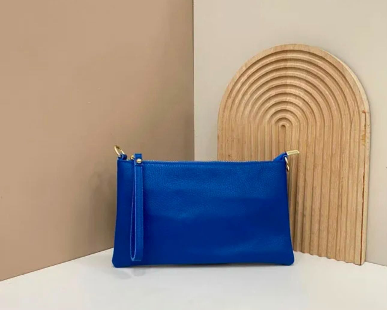 Un estuche azul con cremallera sobre una superficie blanca, junto a una pieza decorativa de madera curvada